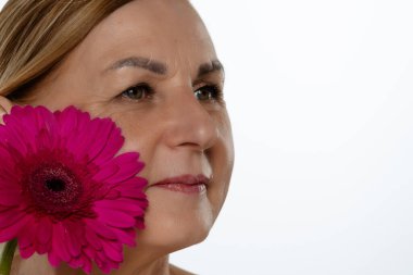Yetişkin bir kadının yüzüne yakın sanatsal bir yaklaşım, gözlerine odaklanmış ve yanında canlı pembe bir çiçek..