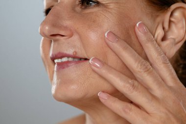 Bir kadının doğal cilt dokusunu gösteren yakın plan bir resim, gülümsemesini ve sağlıklı tenini vurguluyor..