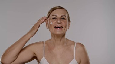 Neşeli bir kadın yaşlanmayı önleyici krem sürüyor, cilt bakımını besleyici su ve tazelikle arttırıyor..