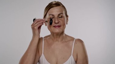 Gecelikli bir kadın yüz silindiri kullanıyor. Bu araç cilt esnekliğini arttırır ve şişkinliği azaltır. Yavaş çekim