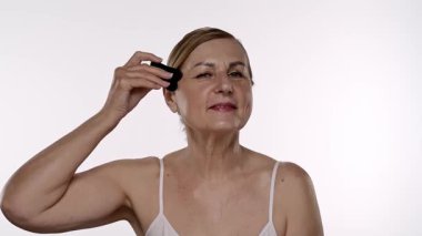 Yaşlı bir kadın yüz masajı için gua sha aleti kullanır, cilt bakımı, rahatlama ve gençleştirme teknikleri gösterir. Yavaş çekim