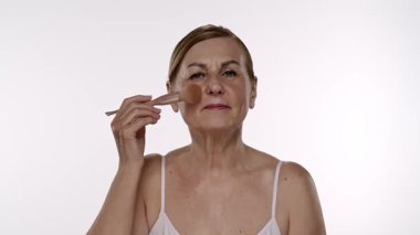 Olgun bir kadın, karmaşık ama doğal bir son için güzellik teknikleri gösteren bir fırça kullanarak makyaj yapar. Yavaş çekim