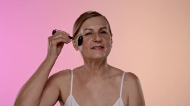 Gecelikli bir kadın yüz silindiri kullanıyor. Bu araç cilt esnekliğini arttırır ve şişkinliği azaltır. Yavaş çekim