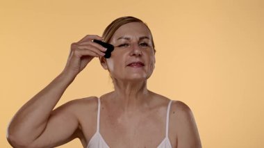 Yaşlı bir kadın yüz masajı için gua sha aleti kullanır, cilt bakımı, rahatlama ve gençleştirme teknikleri gösterir. Yavaş çekim