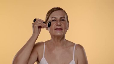 Gecelikli bir kadın yüz silindiri kullanıyor. Bu araç cilt esnekliğini arttırır ve şişkinliği azaltır. Yavaş çekim