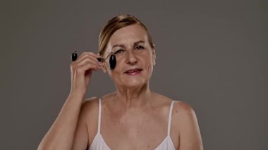 Gecelikli bir kadın yüz silindiri kullanıyor. Bu araç cilt esnekliğini arttırır ve şişkinliği azaltır. Yavaş çekim