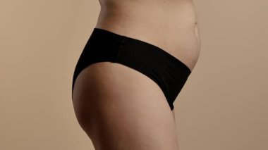 Tarafsız bir arka planda bir kadının kalçasının ve kalçasının detaylı görüntüsü. Kadın siyah, pürüzsüz iç çamaşırı giyiyor. Yaklaşın, ağır çekim.
