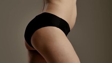 Tarafsız bir arka planda bir kadının kalçasının ve kalçasının detaylı görüntüsü. Kadın siyah, pürüzsüz iç çamaşırı giyiyor. Yaklaşın, ağır çekim.