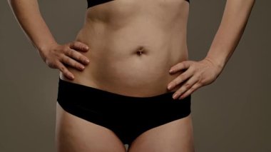 Orta kısımda siyah iç çamaşırlarıyla karnını aydınlatan bir kadının yakın çekim görüntüsü. Yavaş çekim