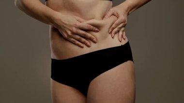 Bir insanın karın derisini çimdiklediği, doku ve yapısına odaklandığı yakın plan bir görüntü. Yavaş çekim