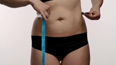 Siyah iç çamaşırlı bir kadın bel ölçüsünü mavi bir bantla ölçer, spor ve sağlık hedeflerini sembolize eder. Yaklaşın, ağır çekim.