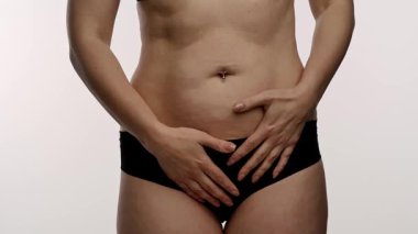 Görüntüde, beyaz bir arkaplana karşı aşkı veya sağlık bilincini sembolize ederek göbeğinde kalp şekli oluşturan bir kadın yer alıyor. Yaklaşın, ağır çekim.