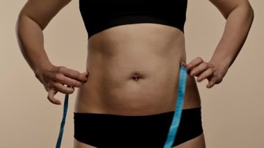 Siyah iç çamaşırlı bir kadın bel ölçüsünü mavi bir bantla ölçer, spor ve sağlık hedeflerini sembolize eder. Yaklaşın, ağır çekim.