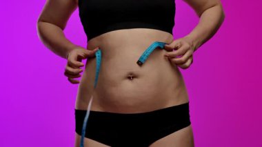 Siyah iç çamaşırlı bir kadın bel ölçüsünü mavi bir bantla ölçer, spor ve sağlık hedeflerini sembolize eder. Yaklaşın, ağır çekim.