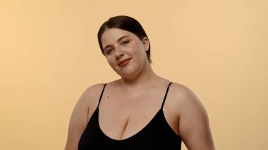 Siyah bluzlu bir kadın tarafsız bir geçmişle güvenle gülümsüyor, basitlik ve zarafet taşıyor..