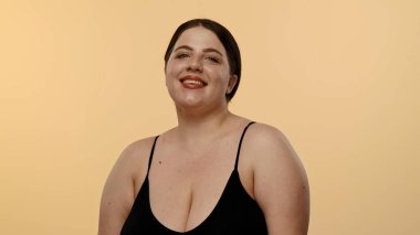 Siyah bluzlu bir kadın tarafsız bir geçmişle güvenle gülümsüyor, basitlik ve zarafet taşıyor..