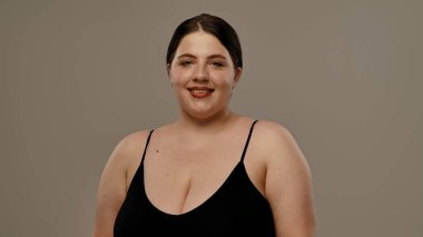 Siyah bluzlu bir kadın tarafsız bir geçmişle güvenle gülümsüyor, basitlik ve zarafet taşıyor..