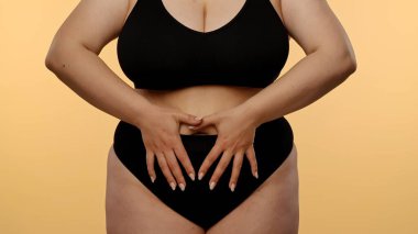 Görüntüde, göbeğinde kalp şekli oluşturan bir kadın var. Tarafsız bir arkaplana karşı sevgi ya da sağlık bilincini simgeliyor..