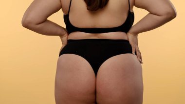 Tarafsız bir arka planda bir kadının kalçasının ve kalçasının detaylı görüntüsü. Kadın siyah, pürüzsüz iç çamaşırı giyiyor..