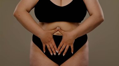 Görüntüde, göbeğinde kalp şekli oluşturan bir kadın var. Tarafsız bir arkaplana karşı sevgi ya da sağlık bilincini simgeliyor..