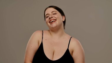 Siyah bluzlu bir kadın tarafsız bir geçmişle güvenle gülümsüyor, basitlik ve zarafet taşıyor..