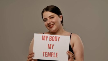 Bir kadın güçlü bir iç çekiş yapıyor Vücudum Tapınağım vücudum pozitifliği destekleyici bir ortamda kişisel gücü ve sevgiyi vurguluyor..