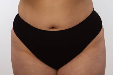 Görüntü, siyah iç çamaşırı giyen bir kişinin basit bir arkaplan karşısında orta kısma odaklandığını gösteriyor..