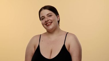 Siyah bluzlu bir kadın tarafsız bir geçmişle güvenle gülümsüyor, basitlik ve zarafet taşıyor. Yavaş çekim