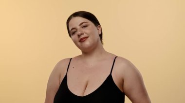 Siyah bluzlu bir kadın tarafsız bir geçmişle güvenle gülümsüyor, basitlik ve zarafet taşıyor. Yavaş çekim