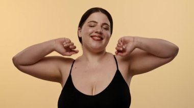 Siyah saçlı neşeli bir kadın gülümserken yüzüne dokunuyor. Arka plan şeftali renginde. Yavaş çekim