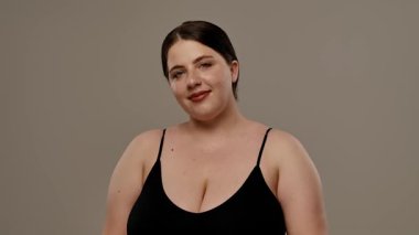 Siyah bluzlu bir kadın tarafsız bir geçmişle güvenle gülümsüyor, basitlik ve zarafet taşıyor. Yavaş çekim