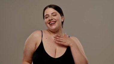 Siyah bluzlu bir kadın tarafsız bir geçmişle güvenle gülümsüyor, basitlik ve zarafet taşıyor. Yavaş çekim