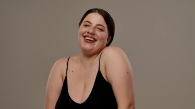 Siyah bluzlu bir kadın tarafsız bir geçmişle güvenle gülümsüyor, basitlik ve zarafet taşıyor. Yavaş çekim