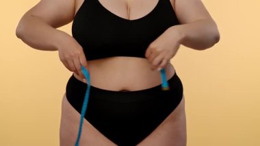 Bir kadın belini bir mezurayla ölçer, spor süreçlerini ve genel sağlık hedeflerini takip etmeye odaklanır. Yavaş çekim