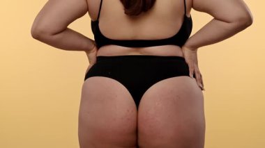 Tarafsız bir arka planda bir kadının kalçasının ve kalçasının detaylı görüntüsü. Kadın siyah, pürüzsüz iç çamaşırı giyiyor. Yavaş çekim