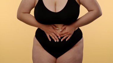 Siyah iç çamaşırı giyen bir kadın midesini tutar. Karın ağrısı ya da ağrı göstergesi olabilir. Yavaş çekim