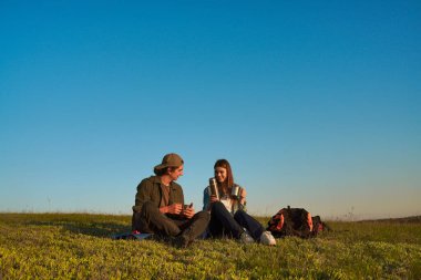 İki genç insan sessiz bir çimenlikte oturur, konuşur, ılık bir içki içer ve doğanın sakin atmosferinin tadını çıkarırlar..