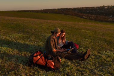 İki genç kampçının dizüstü bilgisayarlarında başarılı bir şekilde güneşli ve manzaralı bir alanda otururken çekilmiş neşeli bir an..