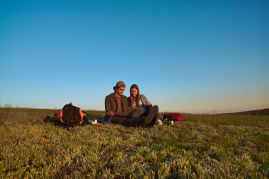 İki genç kampçının dizüstü bilgisayarlarında başarılı bir şekilde güneşli ve manzaralı bir alanda otururken çekilmiş neşeli bir an..