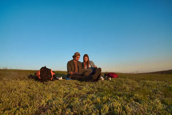 İki genç kampçının dizüstü bilgisayarlarında başarılı bir şekilde güneşli ve manzaralı bir alanda otururken çekilmiş neşeli bir an..