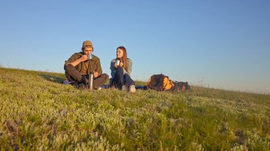 İki genç insan sessiz bir çimenlikte oturur, konuşur, ılık bir içki içer ve doğanın sakin atmosferinin tadını çıkarırlar..