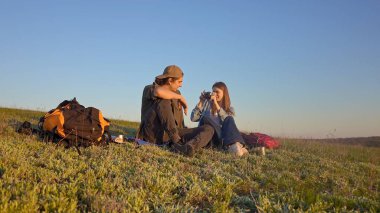 Genç bir çift çimenli bir tepede oturur kamerayla anları yakalar, doğanın güzelliğinin tadını çıkarırlar..