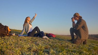 Genç bir çift çimenli bir tepede oturur kamerayla anları yakalar, doğanın güzelliğinin tadını çıkarırlar..