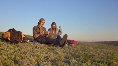 İki genç kampçının dizüstü bilgisayarlarında başarılı bir şekilde güneşli ve manzaralı bir alanda otururken çekilmiş neşeli bir an..