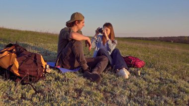 Genç bir çift çimenli bir tepede oturur kamerayla anları yakalar, doğanın güzelliğinin tadını çıkarırlar..