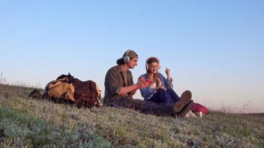 Genç bir çift çimenlerde oturur ve güneşli bir günde açık havada kulaklıklarla müzik dinler..