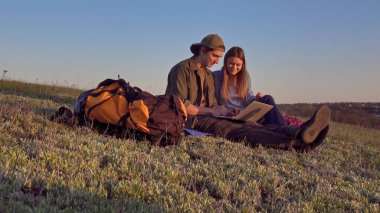 İki genç kampçının dizüstü bilgisayarlarında başarılı bir şekilde güneşli ve manzaralı bir alanda otururken çekilmiş neşeli bir an..