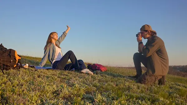 Genç bir çift çimenli bir tepede oturur kamerayla anları yakalar, doğanın güzelliğinin tadını çıkarırlar..