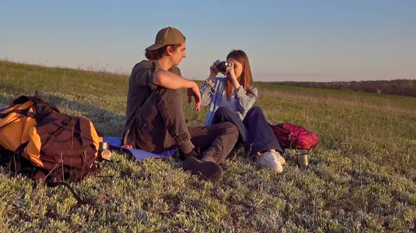 Genç bir çift çimenli bir tepede oturur kamerayla anları yakalar, doğanın güzelliğinin tadını çıkarırlar..