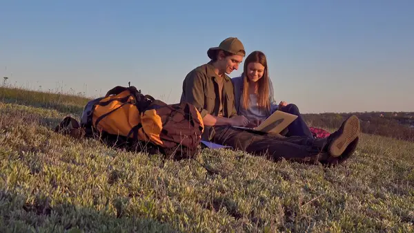 İki genç kampçının dizüstü bilgisayarlarında başarılı bir şekilde güneşli ve manzaralı bir alanda otururken çekilmiş neşeli bir an..